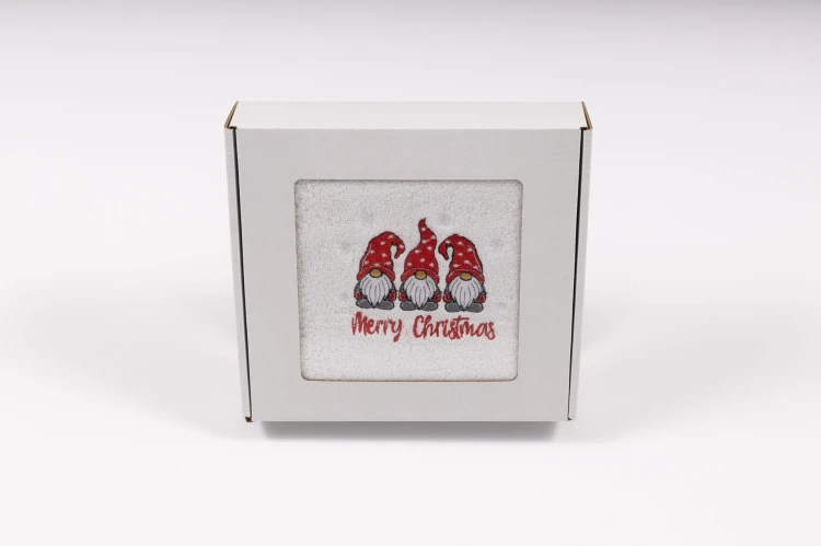 Elegancki świąteczny ręcznik frotte 500g z precyzyjnym haftem przedstawiającym trzy urocze krasnale i napis Merry Christmas, zapakowany w białe kartonowe pudełko z okienkiem, idealny na prezent pod choinkę.