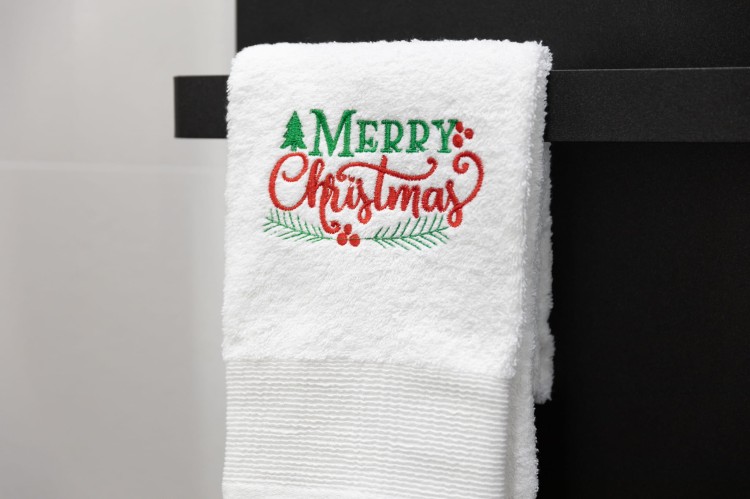 Miękki, bawełniany ręcznik bożonarodzeniowy z napisem Merry Christmas, powieszony na wieszaku w nastrojowej łazience jako świąteczna dekoracja wnętrza.
