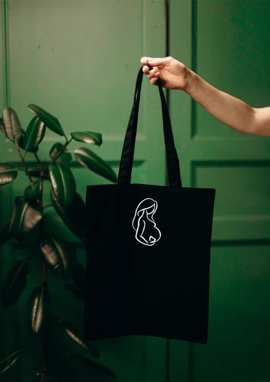 Czarna torba bawełniana z czarnym haftem przedstawiającym sylwetkę kobiety w ciąży z czerwonym serduszkiem na brzuchu.