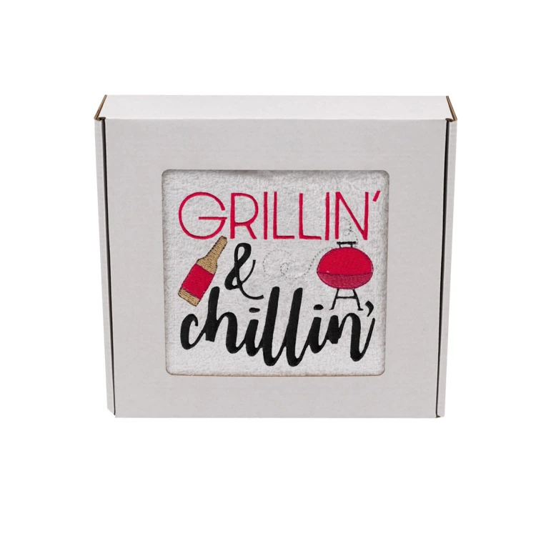 Biały ręcznik z haftem Grillin' and chilliin', zapakowany w białe pudełko z okienkiem.