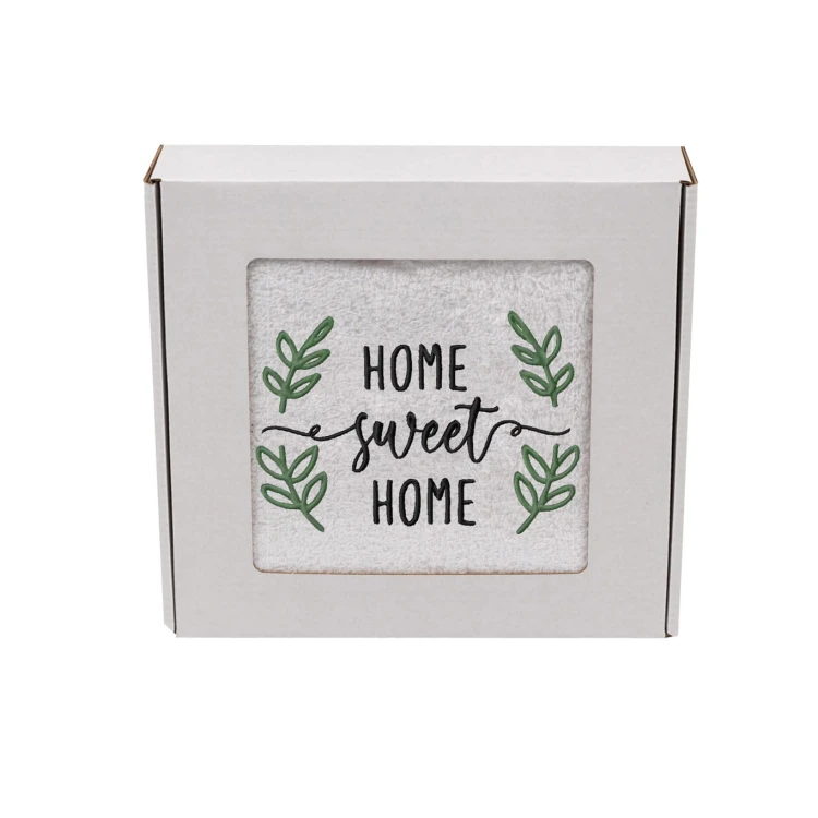 Biały ręcznik z haftem Home Sweet Home zapakowany w ozdobne białe pudełko z okienkiem prezentowym.