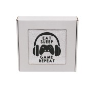 Gamingowy ręcznik z haftem pad, słuchawki i napis Eat Sleep Game Repeat zapakowany w ozdobne prezentowe pudełko z okienkiem.