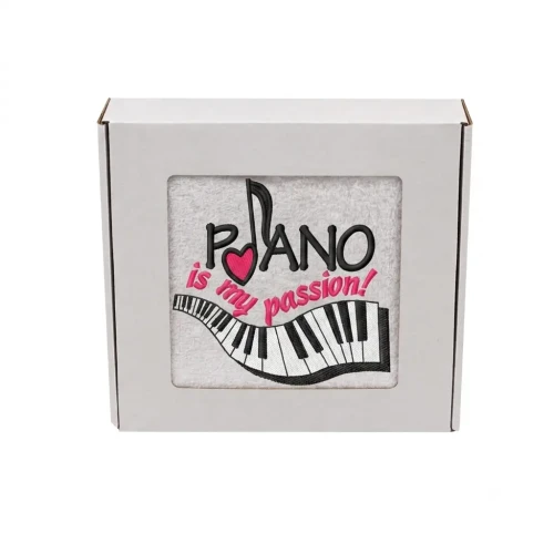 Biały ręcznik bawełniany z haftem przedstawiającym klawiaturę fortepianu, nutę z różowym sercem i napis Piano is my passion, zapakowany w ozdobne pudełko z okienkiem.