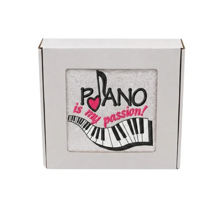 Biały ręcznik bawełniany z haftem przedstawiającym klawiaturę fortepianu, nutę z różowym sercem i napis Piano is my passion, zapakowany w ozdobne pudełko z okienkiem.