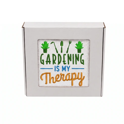 Biały ręcznik z kolorowym haftem Gardening is My Therapy i motywem narzędzi ogrodniczych, zapakowany w prezentowe pudełko z okienkiem.