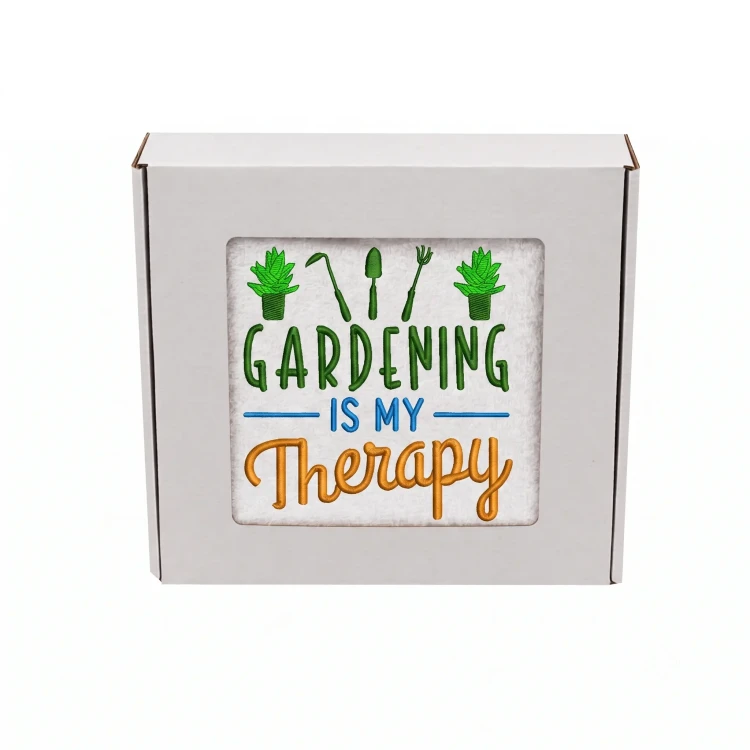 Biały ręcznik z kolorowym haftem Gardening is My Therapy i motywem narzędzi ogrodniczych, zapakowany w prezentowe pudełko z okienkiem.