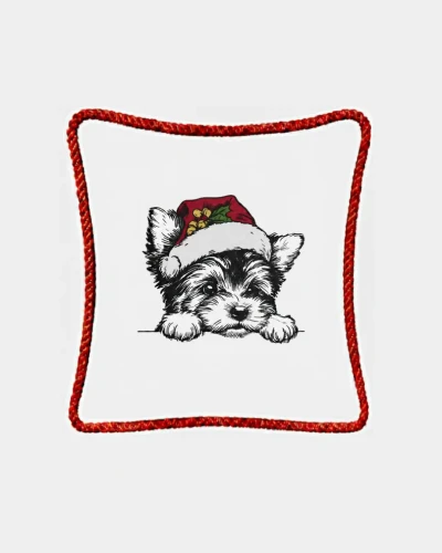 Śmietankowa poszewka welurowa 45x45 cm z haftem przedstawiającym pieska rasy Yorkshire Terrier (York) w świątecznej czapce Mikołaja z gałązką ostrokrzewu, ozdobiona czerwonym sznurem wokół krawędzi.